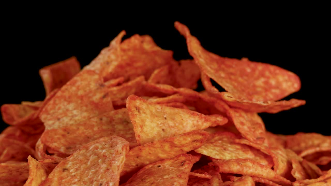 Le tortilla chips dorate ai nachos ruotano sotto le luci dello studio, rivelando la consistenza croccante e i dettagli del condimento