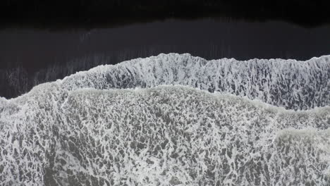 antena: toma de arriba hacia abajo de las olas rompiendo en la playa de arena negra en islandia