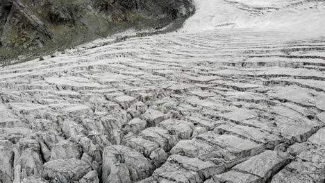 Aerial-flyover-above-the-Moiry-glacier-near-Grimentz-in-Valais,-Switzerland-with-a-pan-down-view-towards-icy-crevasses-cloudy-summer-day