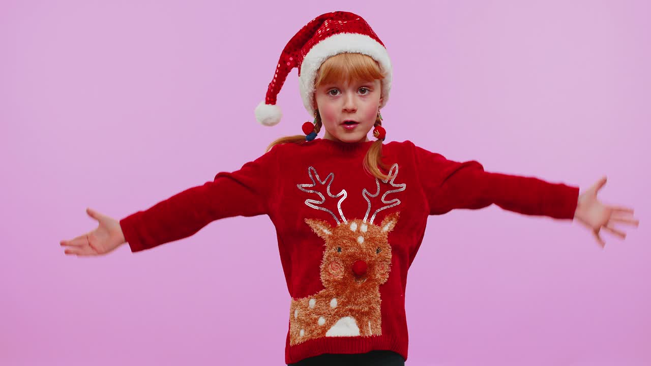 크리스마스 스웨터를 입은 어린 소녀 아이는 갑작스러운 승리에 놀라서 손을 치켜들고, 와우 감정