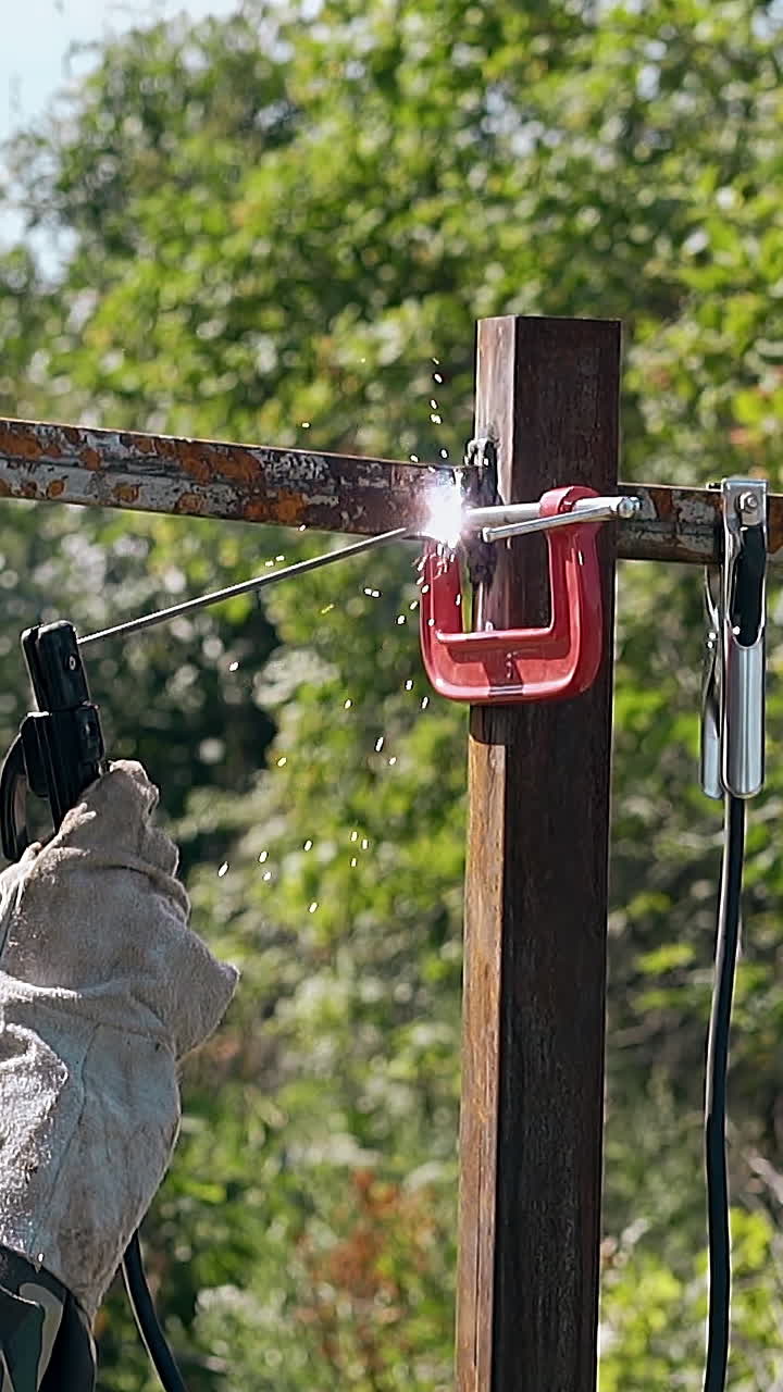 slow motion man in uniform welds and checks fence metal part fixed with new clamp in green yard
