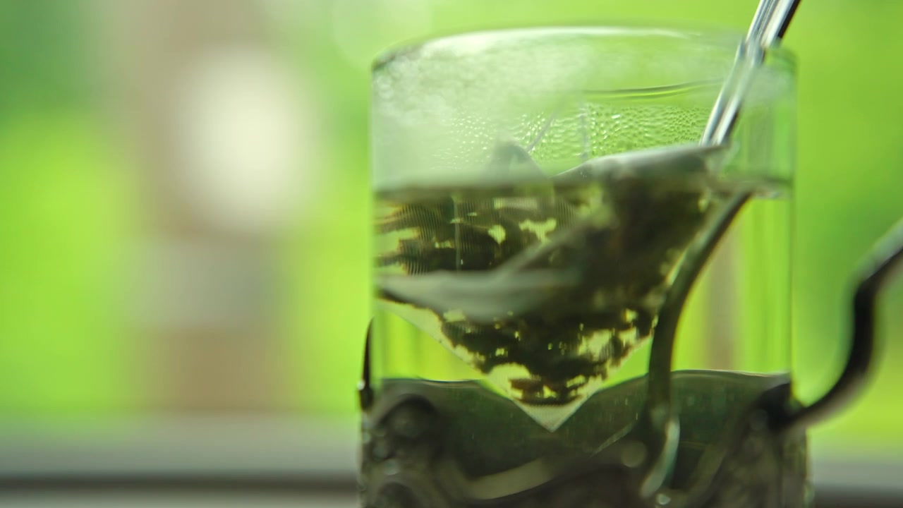 Bustina di tè verde piramidale in infusione in acqua calda in una tazza di vetro