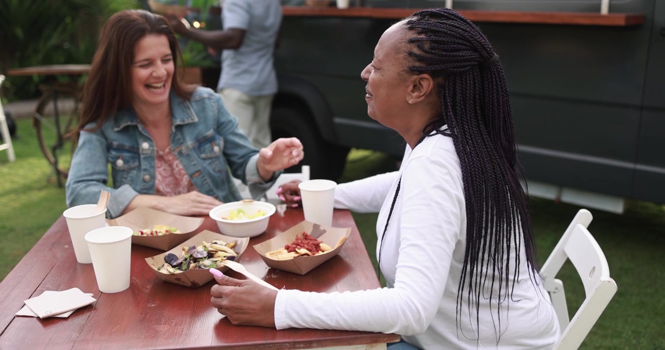 Happy Multiethnic Women Laughing and Eating at Outdoor Food Truck Event