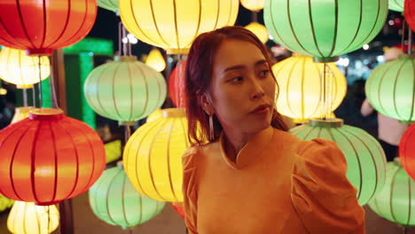 young vietnamese woman in traditional yellow outfit waiting in front of colorful lanterns in hoi an, vietnam