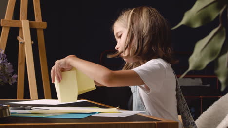 Side-View-Of-Blonde-Girl-Building-Geometrics-Shapes-With-Cardboard-Sitting-At-Desk