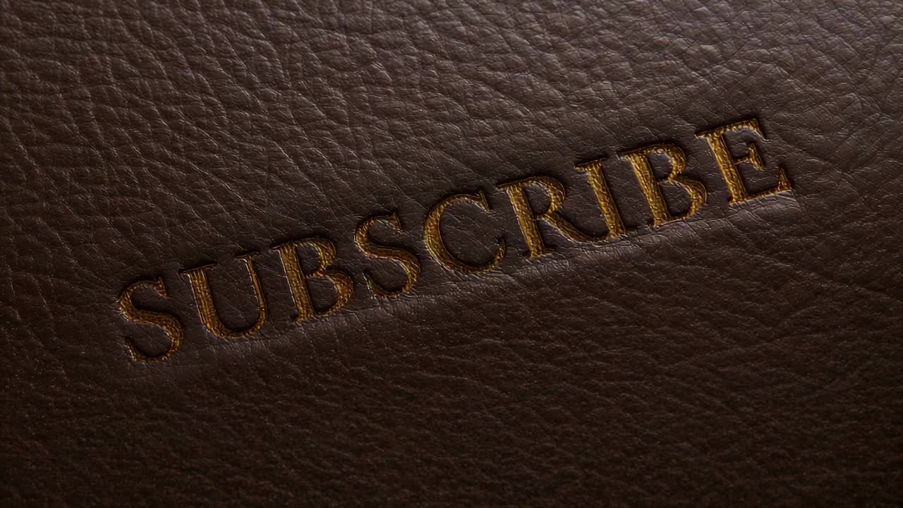 Panning camera right and down showing embossed SUBSCRIBE on leather with warm light revealing grain