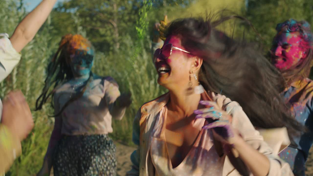 Multi-ethnic group of friends dancing and throwing paint powder enjoying Holi celebration outdoors