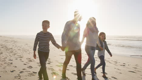 family walking on winter beach holding hands with flaring sun