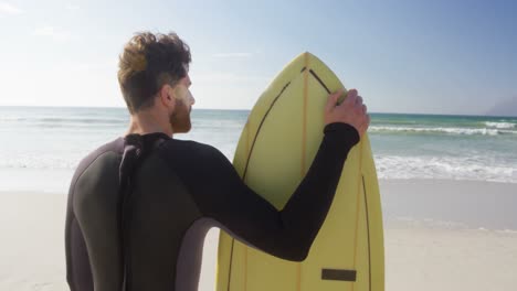 Männlicher-Surfer-Steht-Mit-Surfbrett-Am-Strand-4k