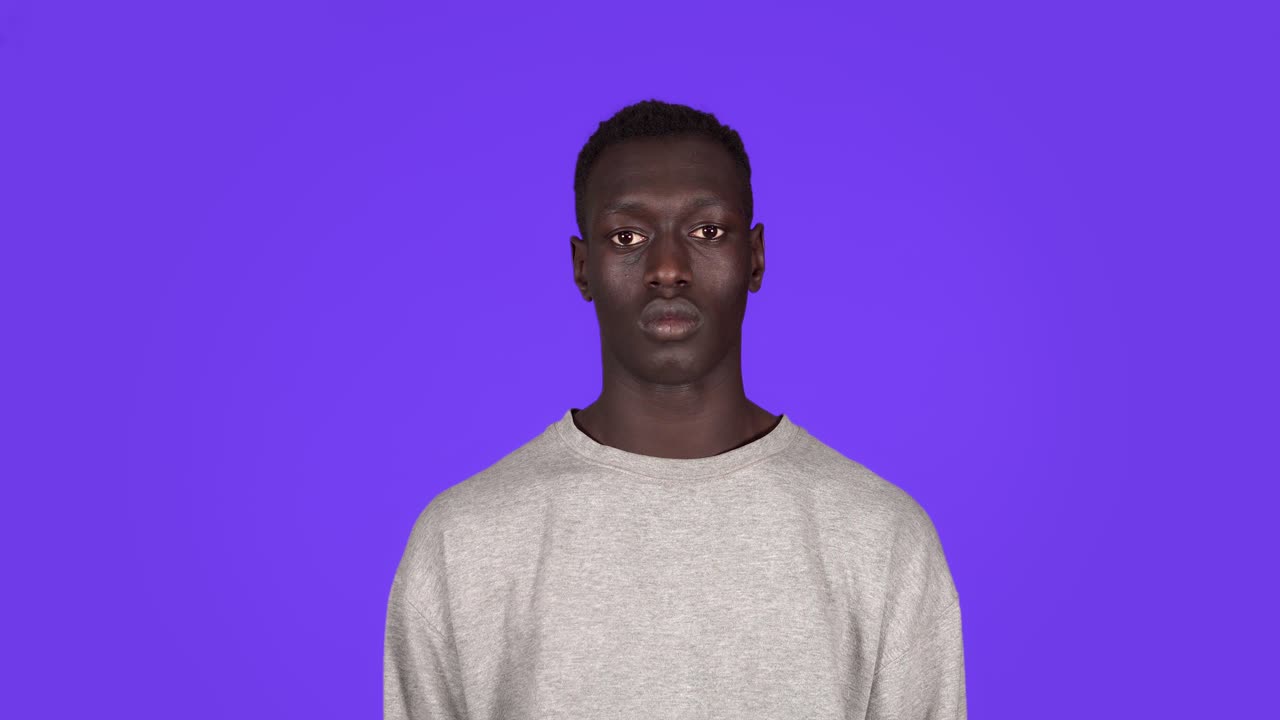Front view portrait of young serious, calm man staring at camera. Beautiful african black man in white sweatshirt on blue background