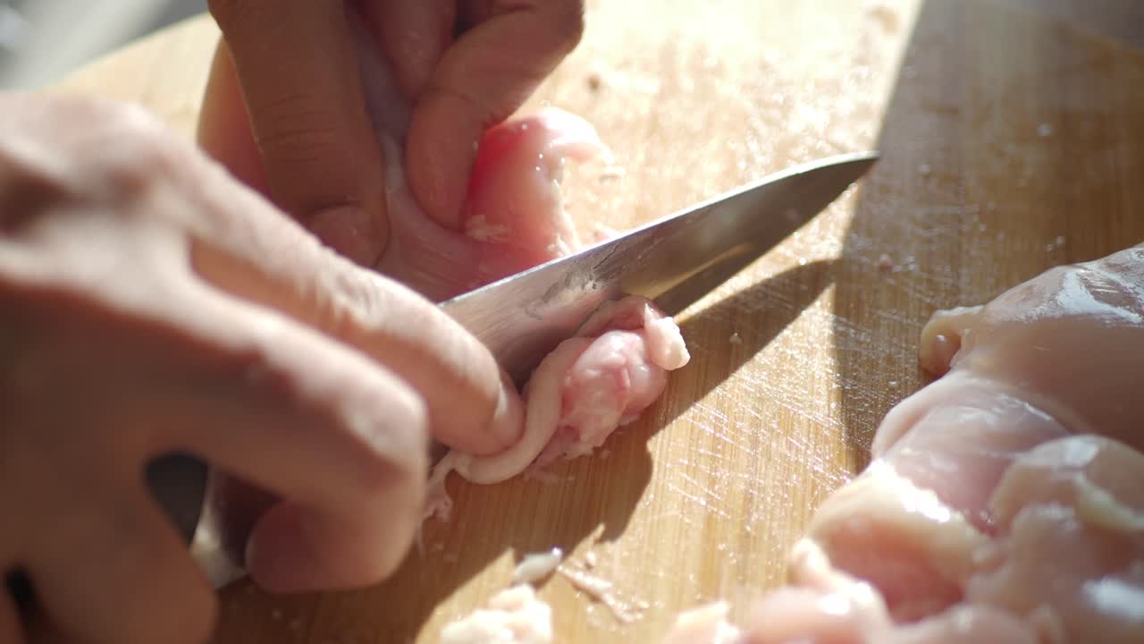 cerca de alguien cortando pecho de pollo crudo en una tabla de cortar