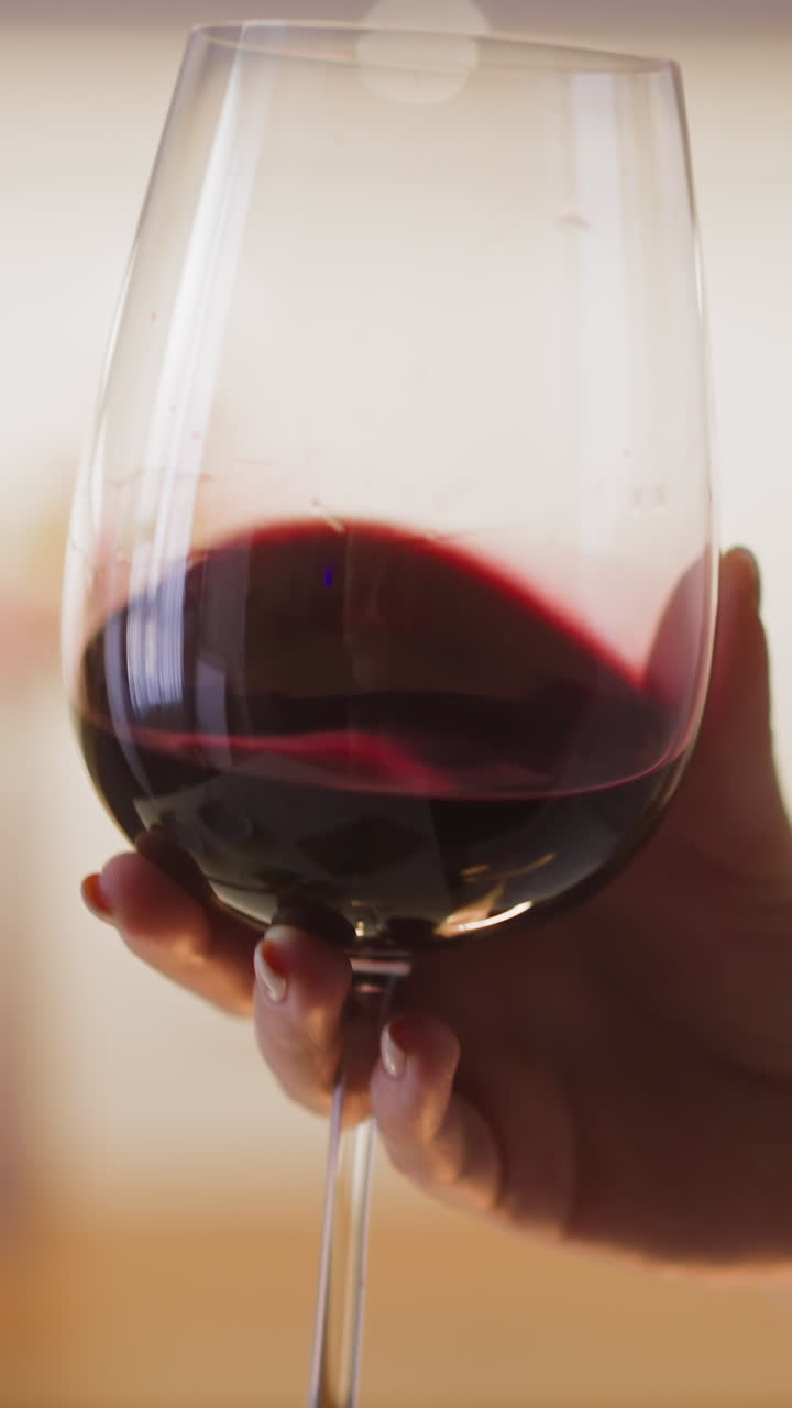 Young woman hand turns elegant large glass with expensive red wine at dinner in spacious kitchen at home extreme close view slow motion