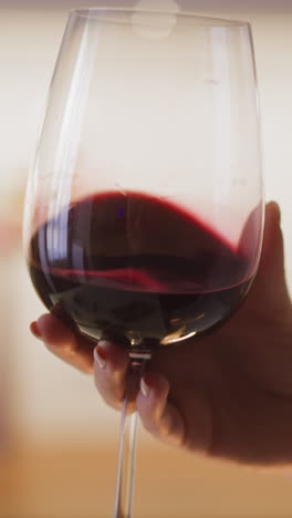 young woman hand turns elegant large glass with expensive red wine at dinner in spacious kitchen at home extreme close view slow motion