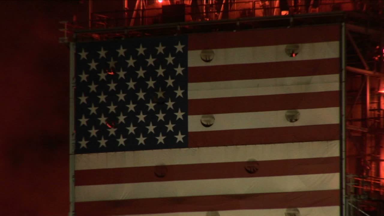 Un murale della bandiera americana decora il lato di una raffineria di petrolio di notte.