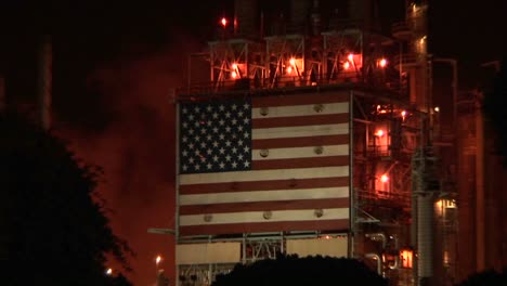 an american flag mural decorates the side of an oil refinery at night