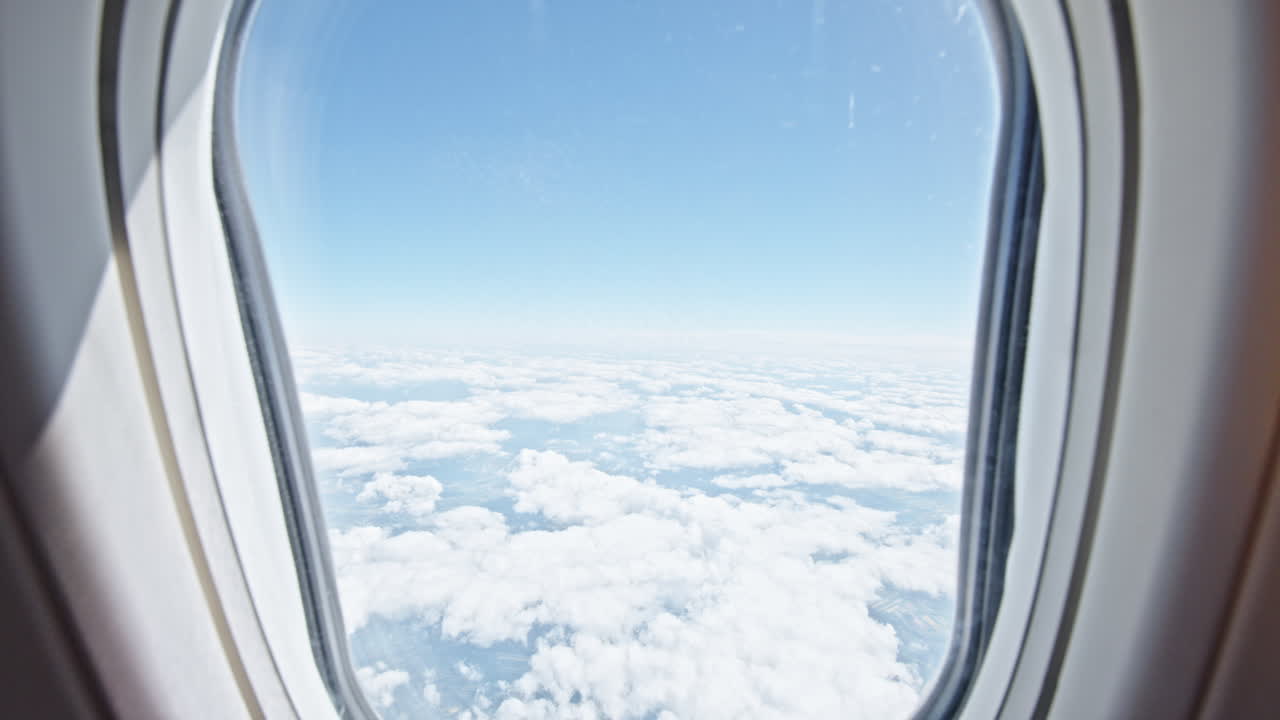 View from an airplane window showing a clear sky with fluffy clouds below