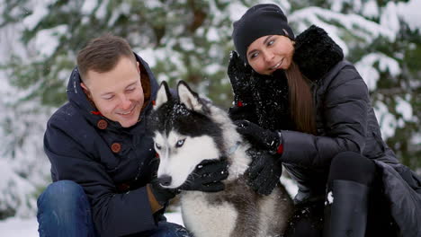 Woman-and-man-play-with-dog-in-snow.