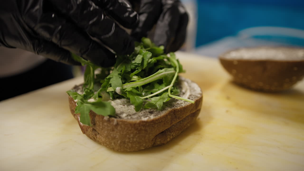 Chef che aggiunge verdure durante la preparazione di un hamburger gourmet.