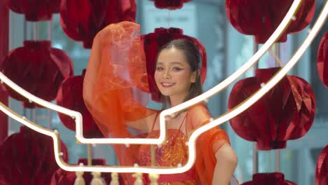 beautiful asian woman wearing traditional red, sleeveless dress poses by the paper lanterns as she celebrates the chinese new year - static slow motion