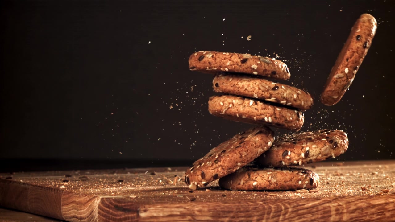 Movimento rallentato di biscotti ai semi che cadono e si accatastano su un tagliere di legno
