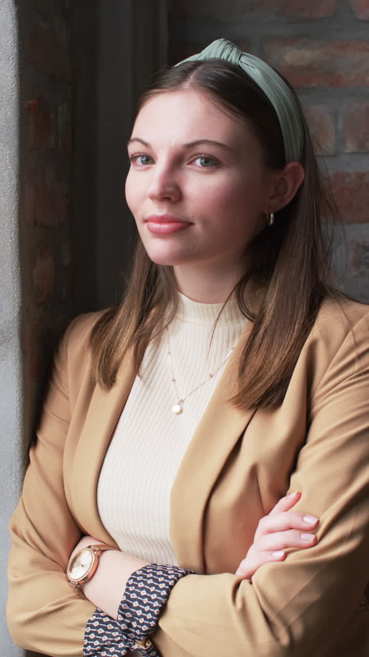 Vertical video: Businesswoman in blazer standing with arms crossed, smiling confidently in office
