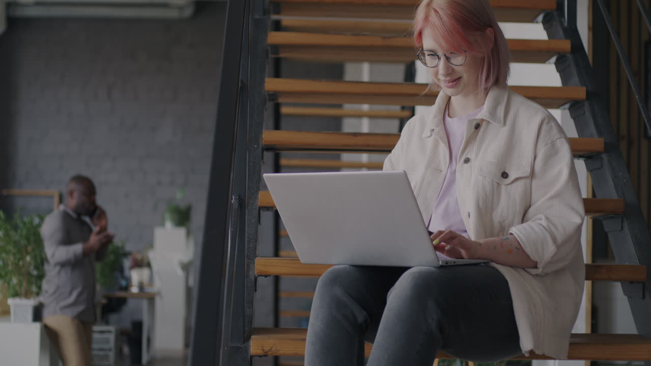Woman Working on Laptop on Stairs in Modern Office