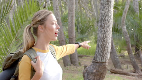 Young-Caucasian-woman-with-a-ponytail-points-at-something-in-a-wooded-area-with-copy-space