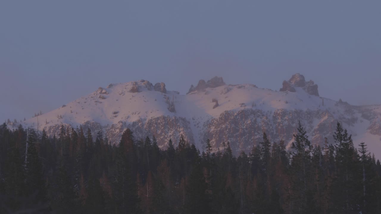 luz de puesta de sol rosa en picos de alta montaña con viento que sopla los árboles en primer plano