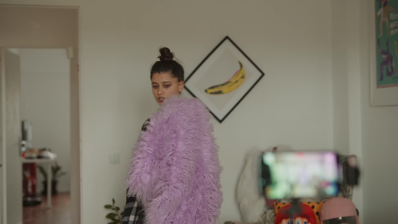 Giovane donna che fa vlogging a casa con lo smartphone e una giacca viola