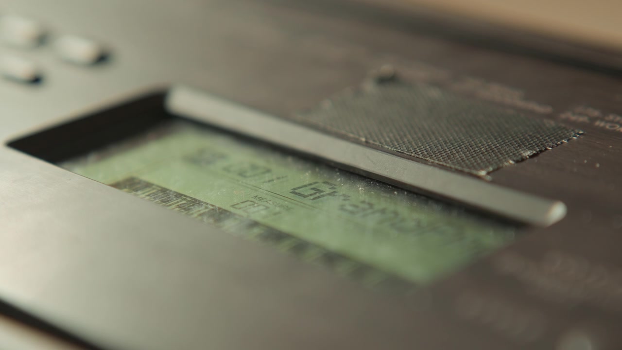 Extreme close view of powered rectangular LCD display recessed inside matte black plastic housing, with faint segmented characters, greenish backlight, subtle motion blur, and clean technical