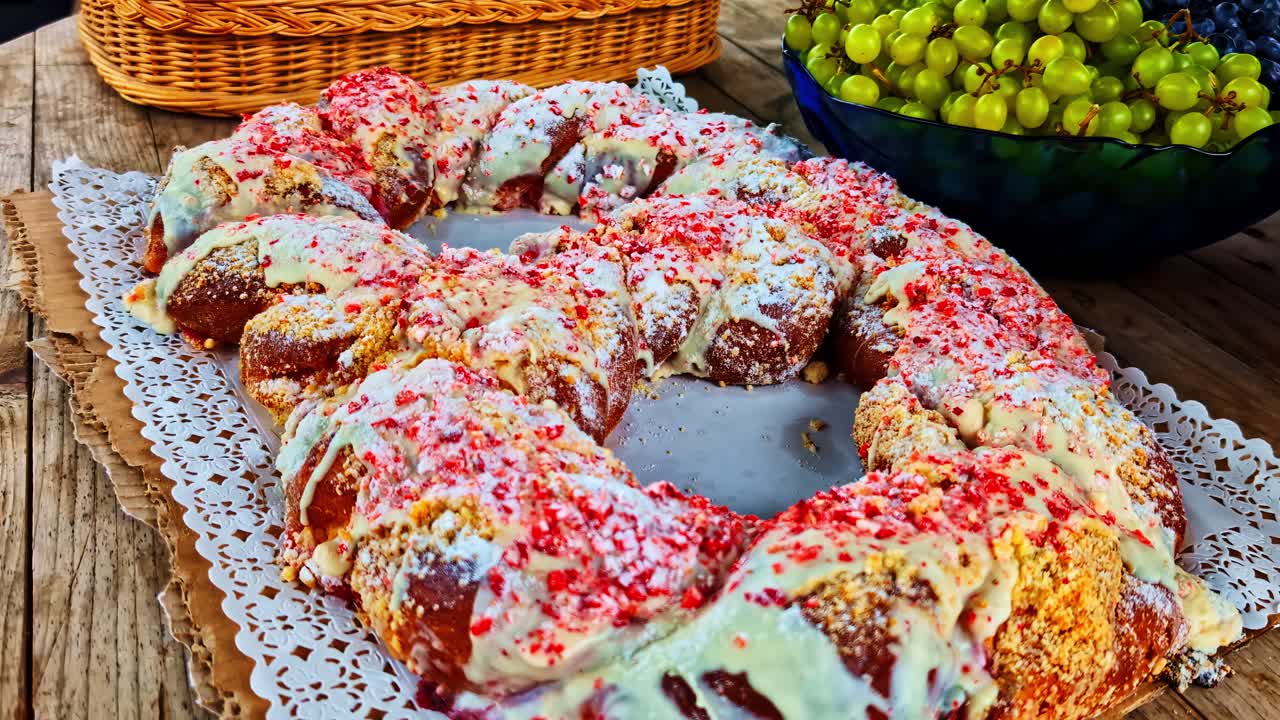 Decorative iced large pretzel pastry ring with sprinkles on lace paper beside grapes in bowl