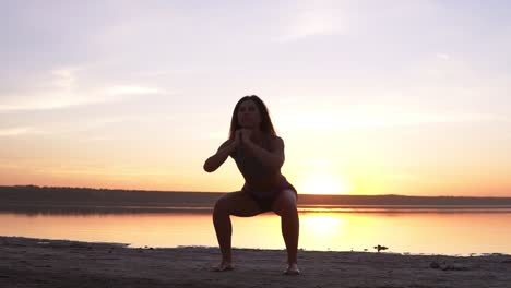 giovane donna attraente che fa esercizi sportivi al mattino sulla spiaggia all'alba vicino al mare o al lago. fa sit-up in abbigliamento sportivo. stile di vita sano, vita attiva, allenamento