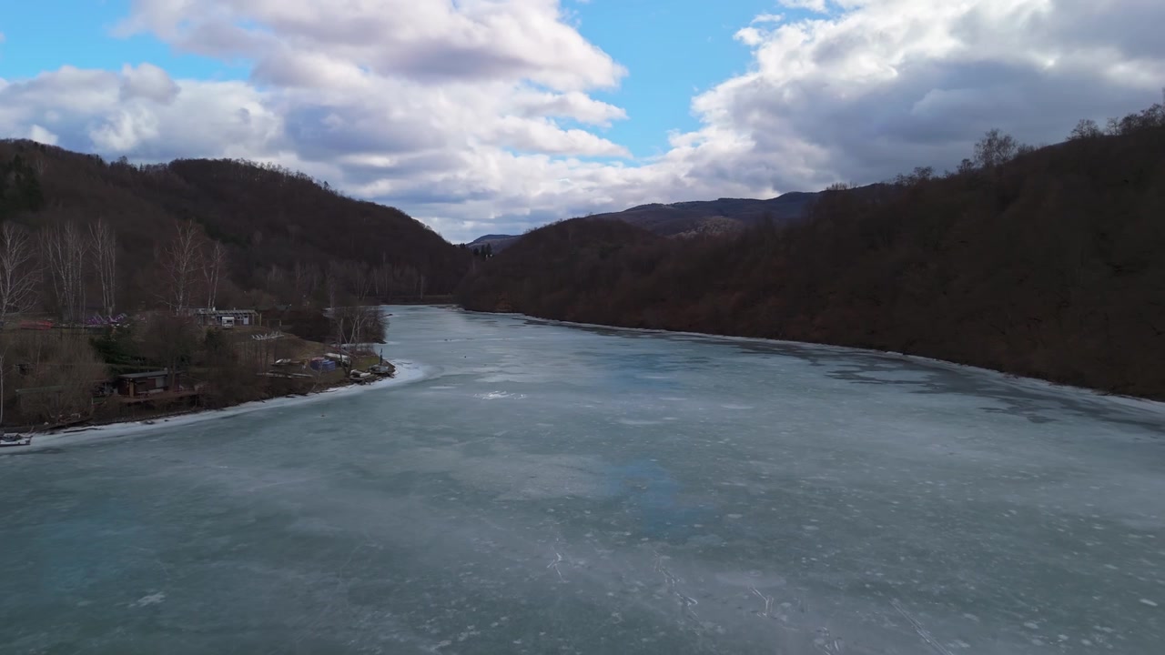 Nella Slovacchia orientale, il bacino idrico di Ružín vicino a Malý Folkmar appare ghiacciato tra montagne, colline e boschi spogli circostanti, visto da un drone in un tranquillo paesaggio invernale.
