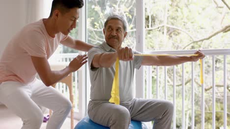 diverse male physiotherapist advising and senior male patient using exercise band, in slow motion