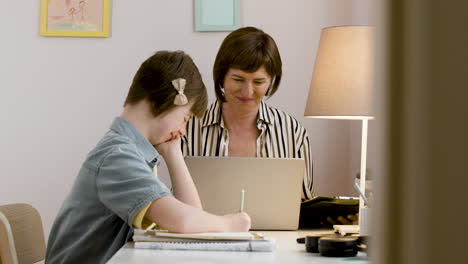 Focused-girl-doing-homework-while-her-mother-works-with-the-laptop