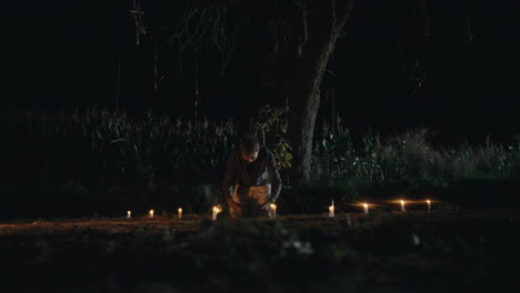 man performing a night ritual under a tree with candles