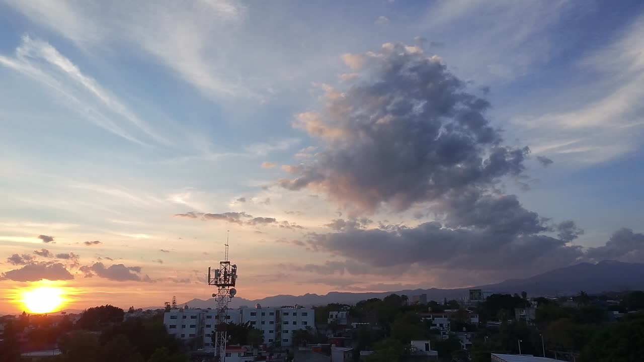 The sun sets over Cuernavaca’s Alameda district, casting golden hues on the cityscape with dramatic cloud formations