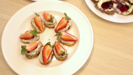 plates on the table containing small sandwiches snacks with strawberry, fish and greens