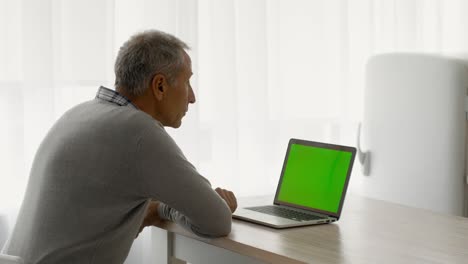 hombre mayor usando una computadora portátil con pantalla clave de croma verde en la cocina