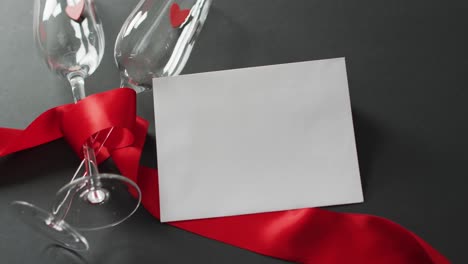 champagne glasses with hearts, red ribbon and white card with copy space at valentine's day