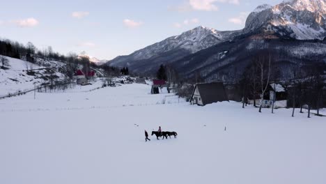 Antena---Gente-Montando-A-Caballo-En-Una-Granja-En-Un-Invierno-Nevado,-Kolasin,-Montenegro,-Pan-Izquierda