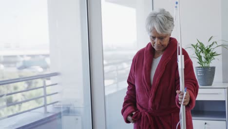 Fröhlicher-älterer-Birazialer-Patient,-Der-Mit-Tropfständer-Am-Fenster-In-Der-Krankenstation-Geht,-Zeitlupe