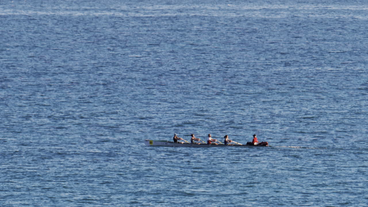 Distant view of a rowing team of four people practicing on calm water, with a coxswain seated at the front