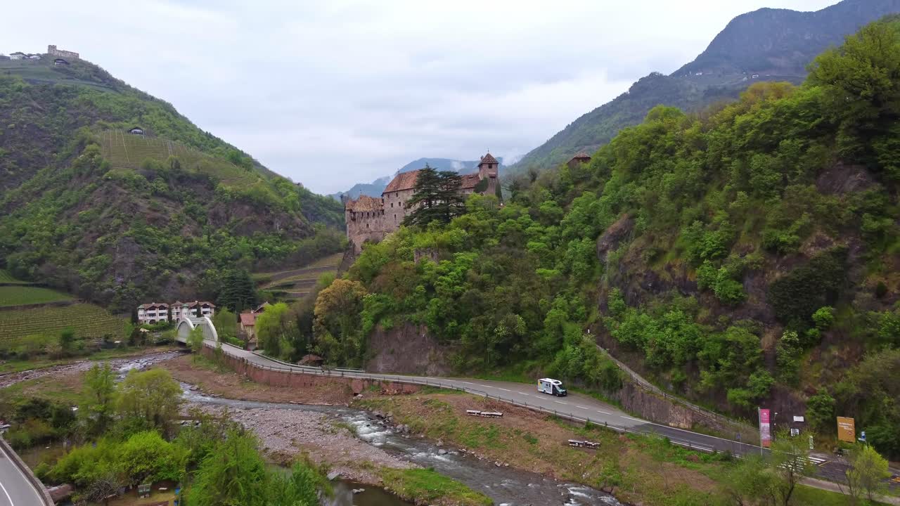 Forward moving aerial reveals Roncolo Castle hidden behind green leaved tree