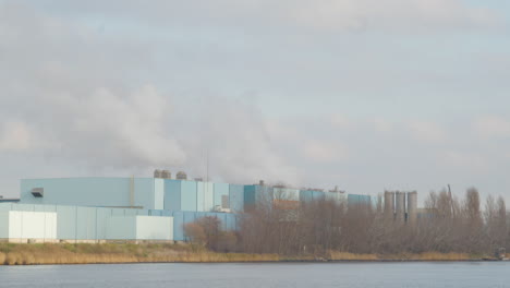 White-smoke-rising-from-industrial-building-on-river-shore---close