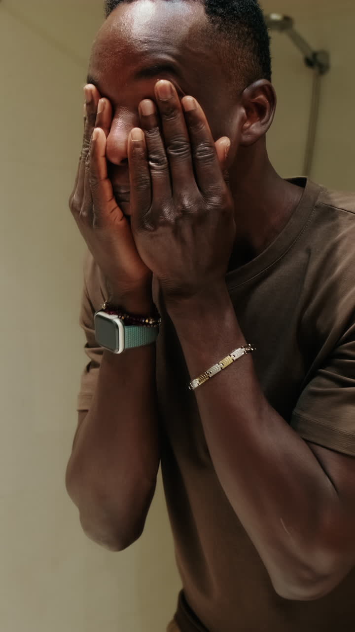 Giovane uomo afroamericano che si lava il viso in bagno