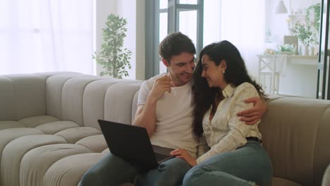 pareja feliz viendo computadora portátil en casa. hombre joven y mujer relajándose en el sofá