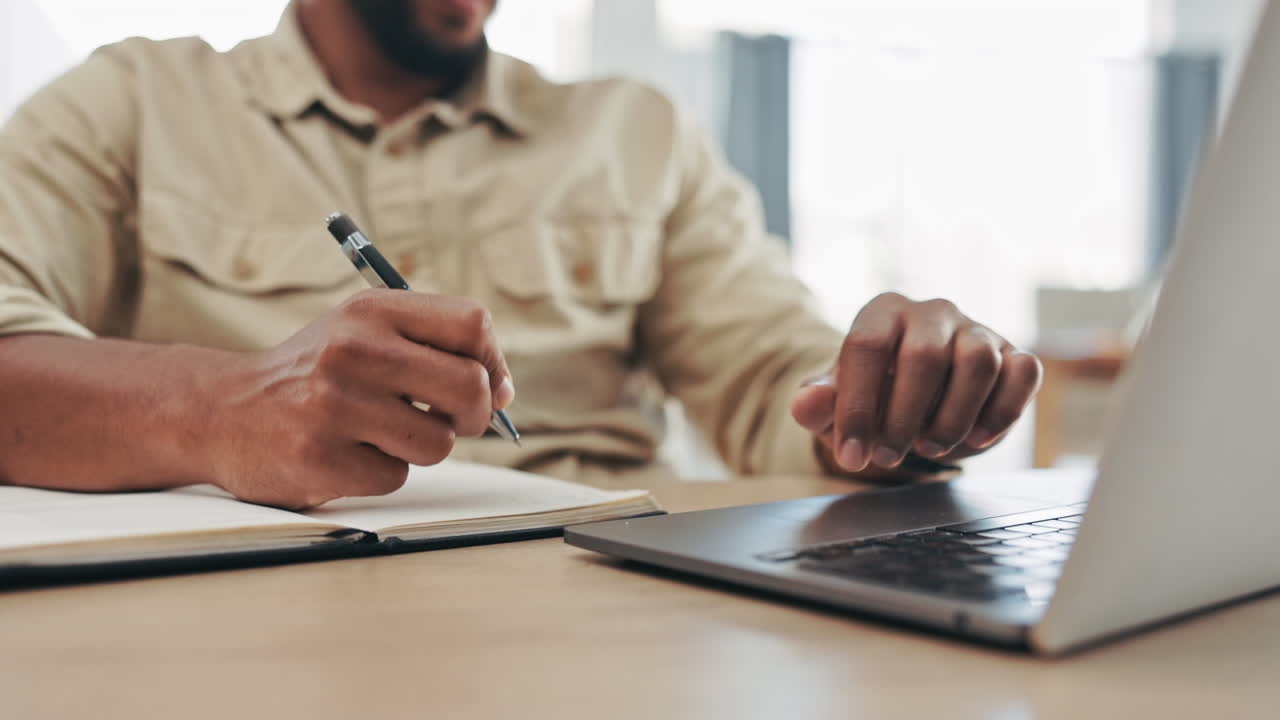 Hands, laptop and a man writing in a notebook