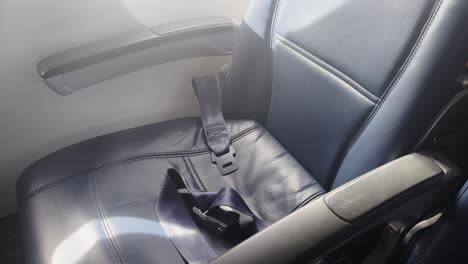 empty plane window seat with unbuckled seatbelt