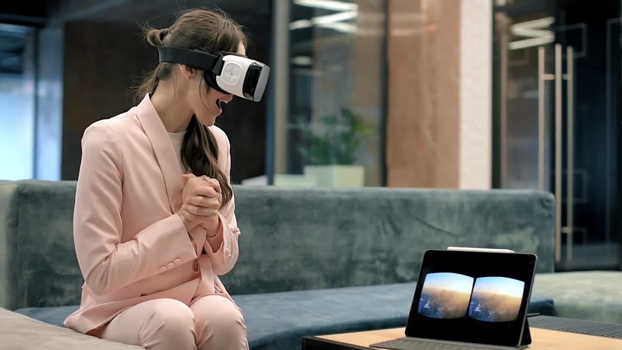 Uma mulher caucasiana loira e animada explorando a realidade virtual com óculos de RV em um escritório. Tablet na mesa mostrando a imagem visível no headset